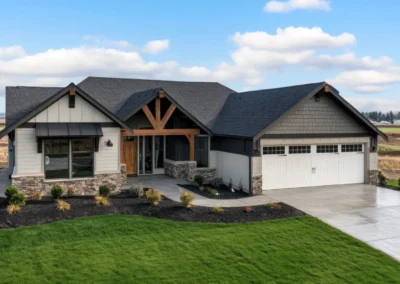 New construction house in Washington state with beautiful landscaping and front yard. The home has a dark brown shingle roof, light gray walls, stone accents on the exterior walls, wooden trim around the windows